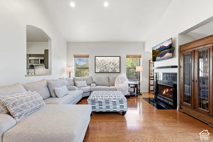 Vaulted ceiling, wood-finish flooring, built-in fireplace with a dark mantel, recessed lighting, and an arched pass-through window