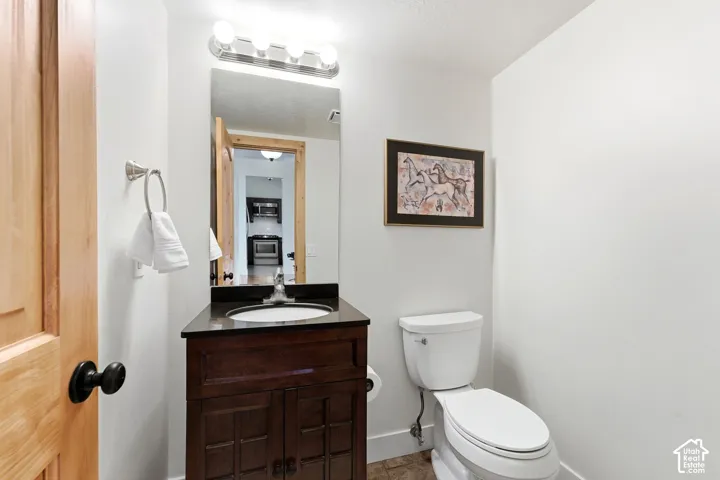 Hardwood door, vanity with dark countertop, white toilet, and tile flooring