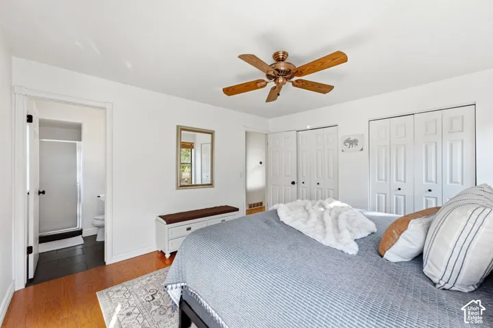 Hardwood-style flooring throughout, ceiling fan with integrated lighting, multiple wardrobe closets, and a private bathroom featuring a glass-enclosed shower and dark tile flooring