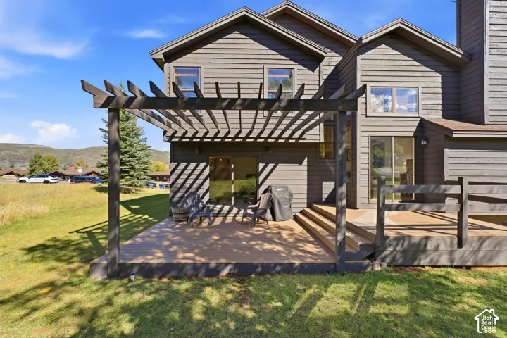 Expansive wood deck with a pergola, featuring multiple sliding glass doors and wood siding