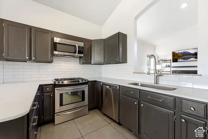 Kitchen featuring dark wood-finish cabinetry, stainless steel appliances, white subway tile backsplash, and light-toned countertops