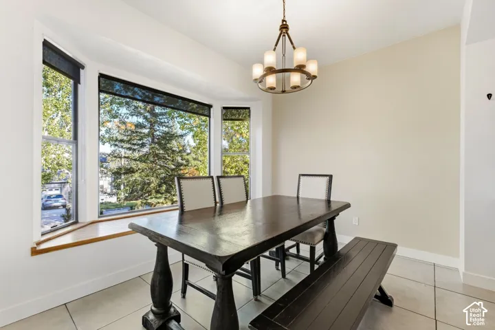 Bay window with a wood-finish sill, ring chandelier with frosted glass shades, and tile flooring