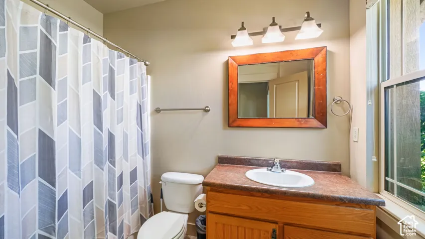 Bathroom featuring a wood-finish vanity with an integrated sink, three-light vanity fixture, and a window with a slatted design