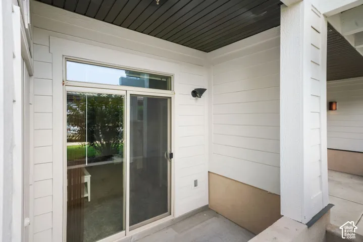 Sliding glass door with transom window, concrete patio, exterior wall sconce, and white horizontal siding