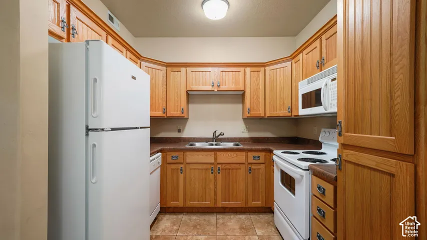 Kitchen featuring wood cabinetry, white appliances, a built-in microwave, a double basin sink, and tile flooring