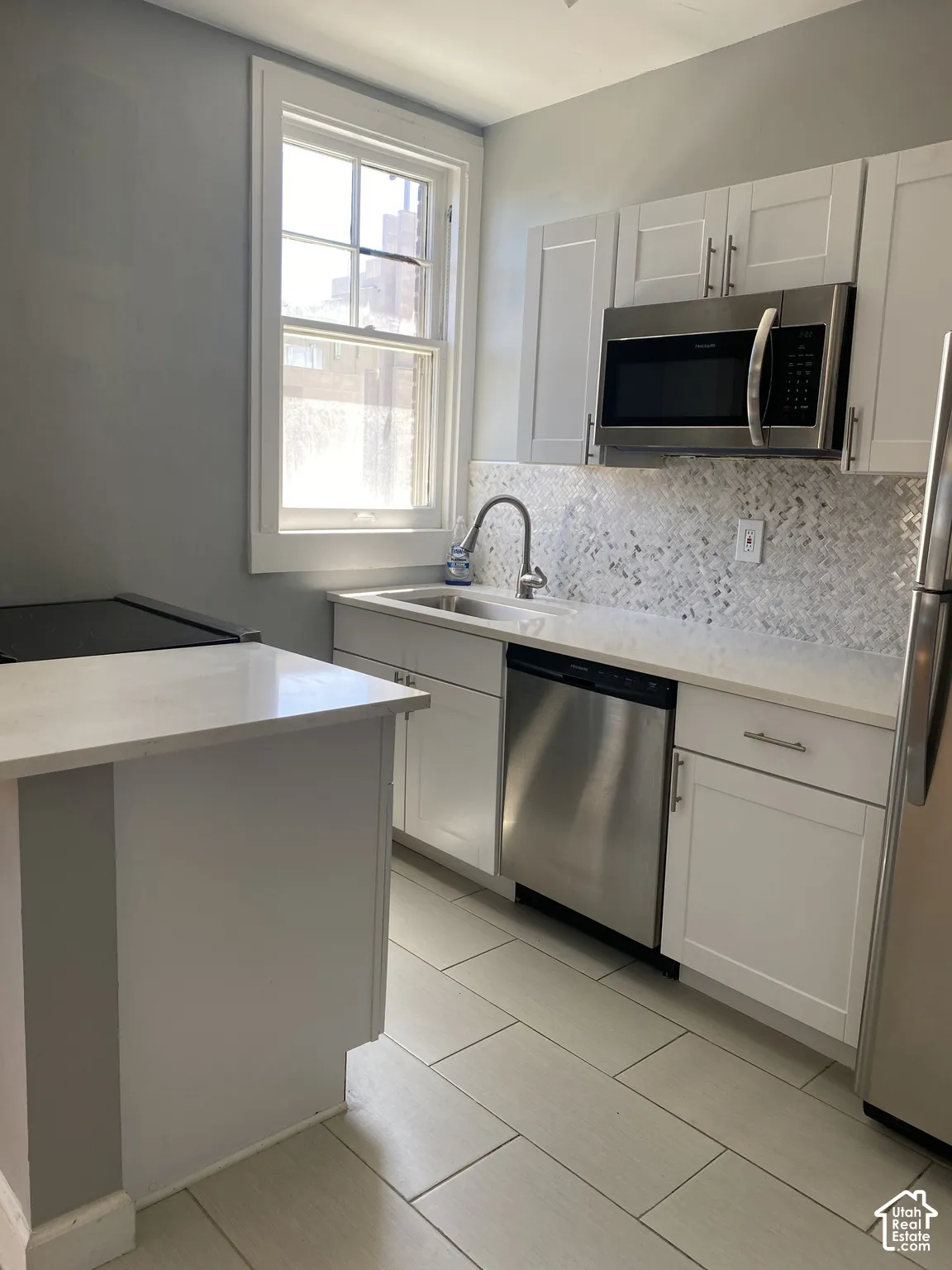 Kitchen featuring white shaker cabinetry, stainless steel appliances, light-toned countertops, a patterned tile backsplash, and light-toned tile flooring