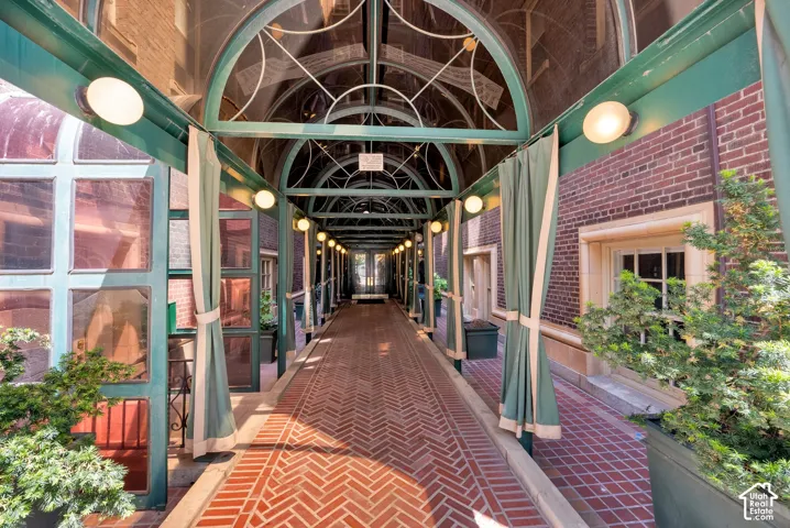 Covered walkway with arched metal framework, herringbone brick flooring, and wall-mounted lighting