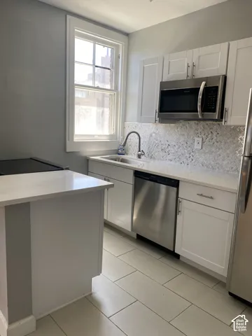 Kitchen featuring white shaker cabinetry, stainless steel appliances, light-toned countertops, a patterned tile backsplash, and light-toned tile flooring