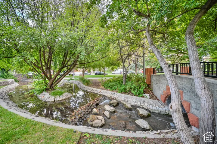 Manicured green spaces featuring a winding water feature with stone edging, mature shade trees, and a black metal railing