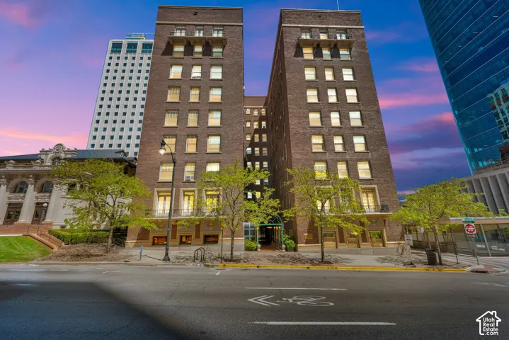 Brick facade building with multiple levels, featuring street-level entry, established trees, and surrounding urban architecture