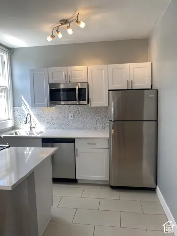 Kitchen featuring white shaker cabinetry, stainless steel appliances, light-toned countertops, tile backsplash, and track lighting