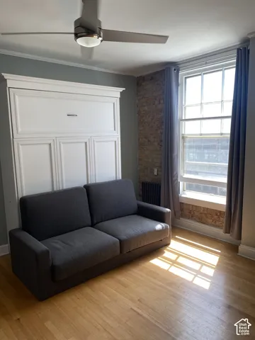 Integrated wall bed system with panel detailing, light wood-finish flooring, exposed brick accent wall, and a ceiling fan with integrated lighting