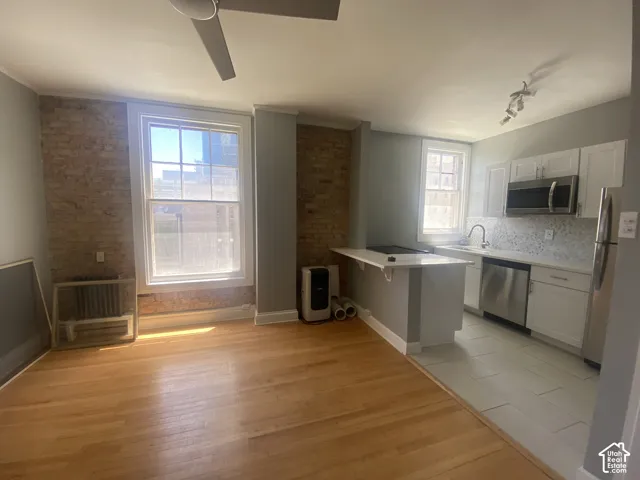 Hardwood flooring, exposed brick wall, white shaker cabinetry, stainless steel appliances, and a breakfast bar