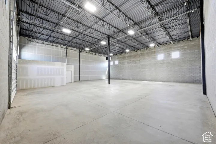 Spacious concrete flooring with high ceilings, exposed metal truss system, multiple recessed lighting fixtures, and concrete block walls