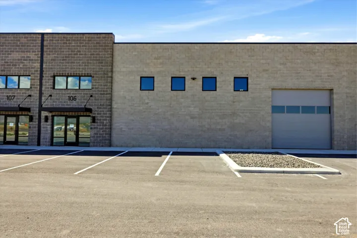 Commercial building featuring brick and concrete block construction, multiple storefront entries with glass doors, prominent overhead door, and paved parking area