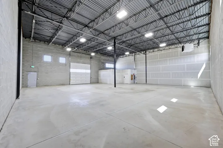 Spacious commercial interior featuring a concrete floor, high exposed metal ceiling, multiple overhead lighting fixtures, and a large roll-up door