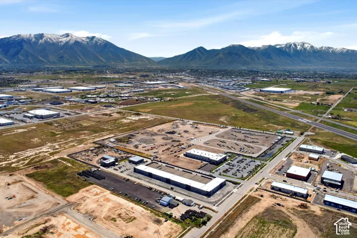 Expansive industrial area with multiple commercial buildings, paved roadways, and ample parking, set against a backdrop of distant mountains