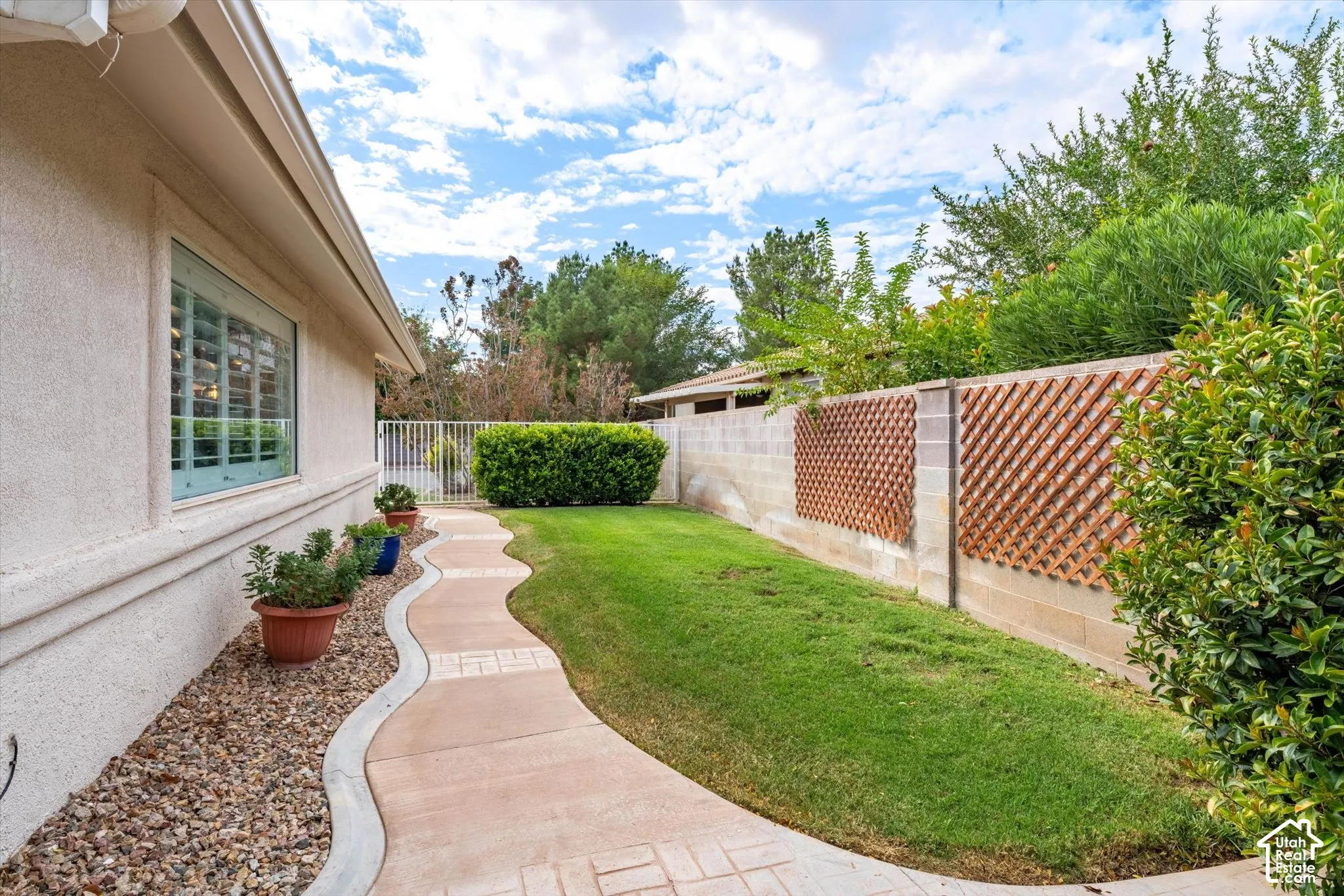 Exterior stucco finish, decorative window shutters, landscaped gravel bed, winding concrete pathway, and a block wall with lattice accents