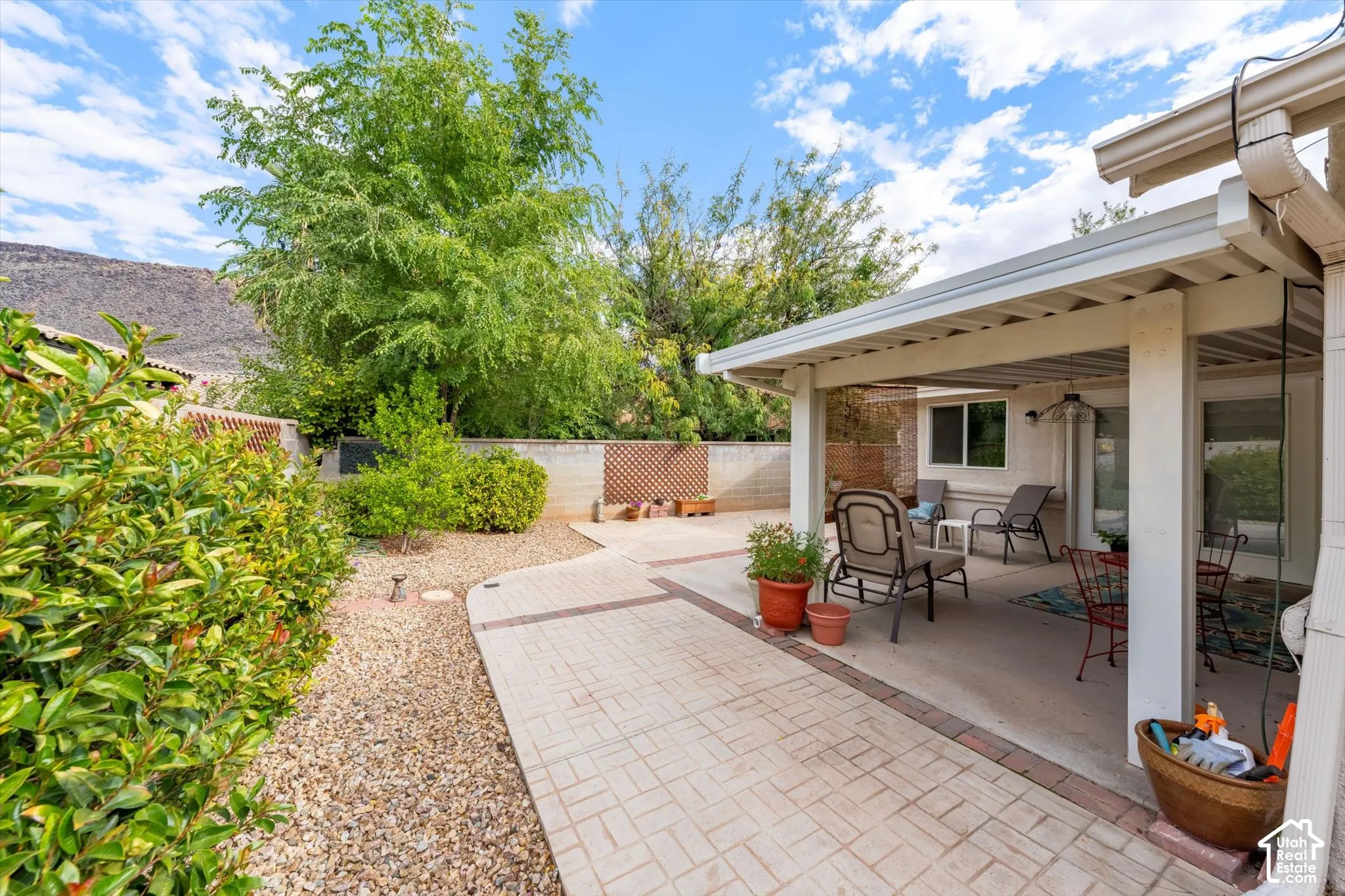 Covered patio featuring a ceiling fan, concrete flooring, and an adjacent patterned stone paver walkway