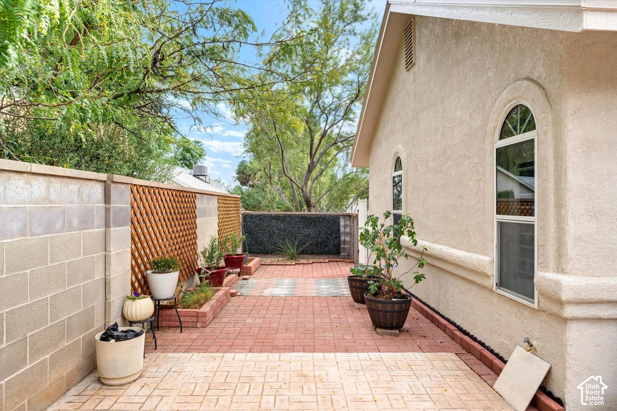 Stucco exterior with arched windows, brick paver patio, raised garden beds, and block wall fencing with wood lattice accents