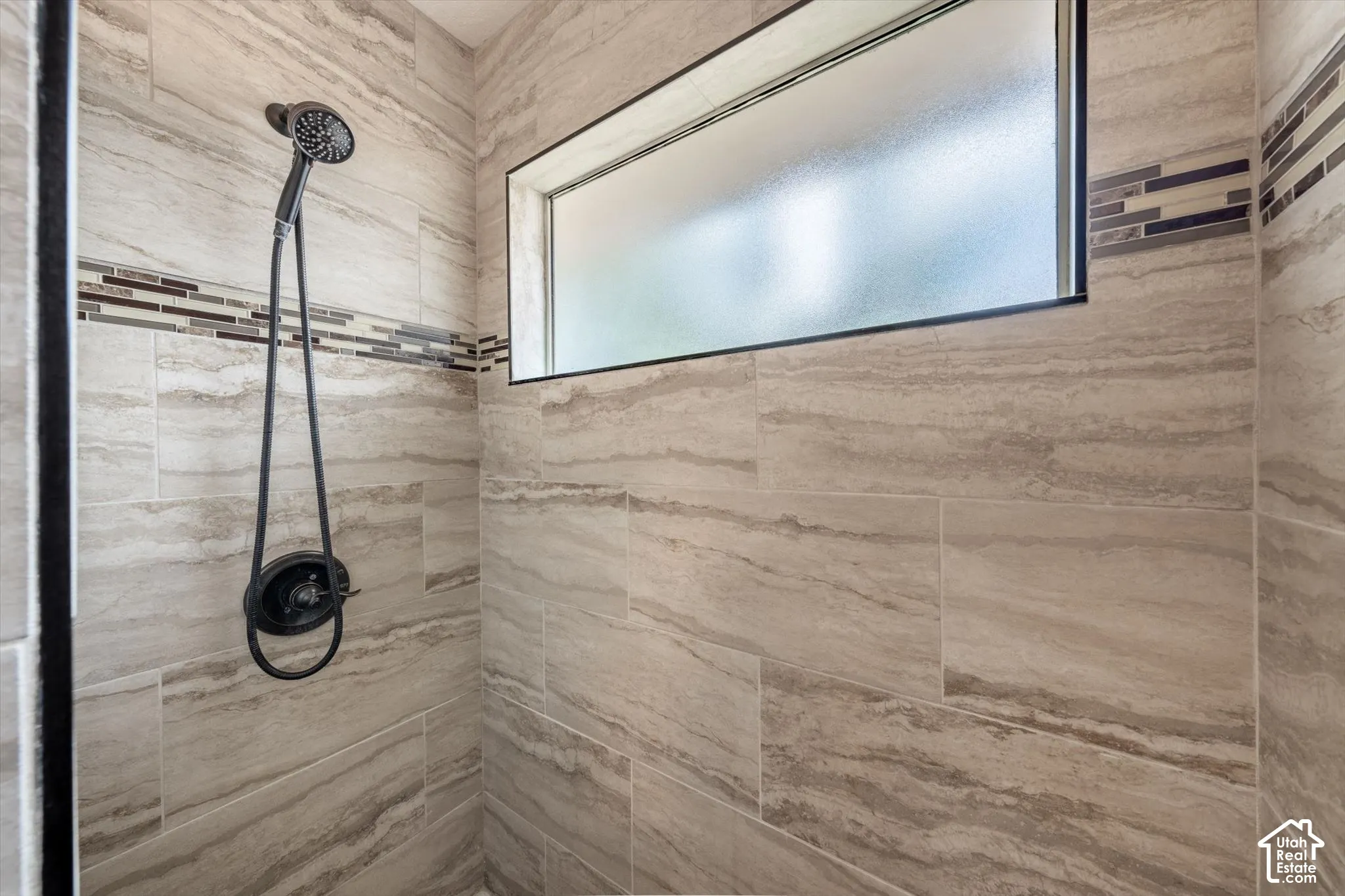 Shower enclosure featuring large format tile, mosaic accent band, matte black shower fixtures, and a transom window