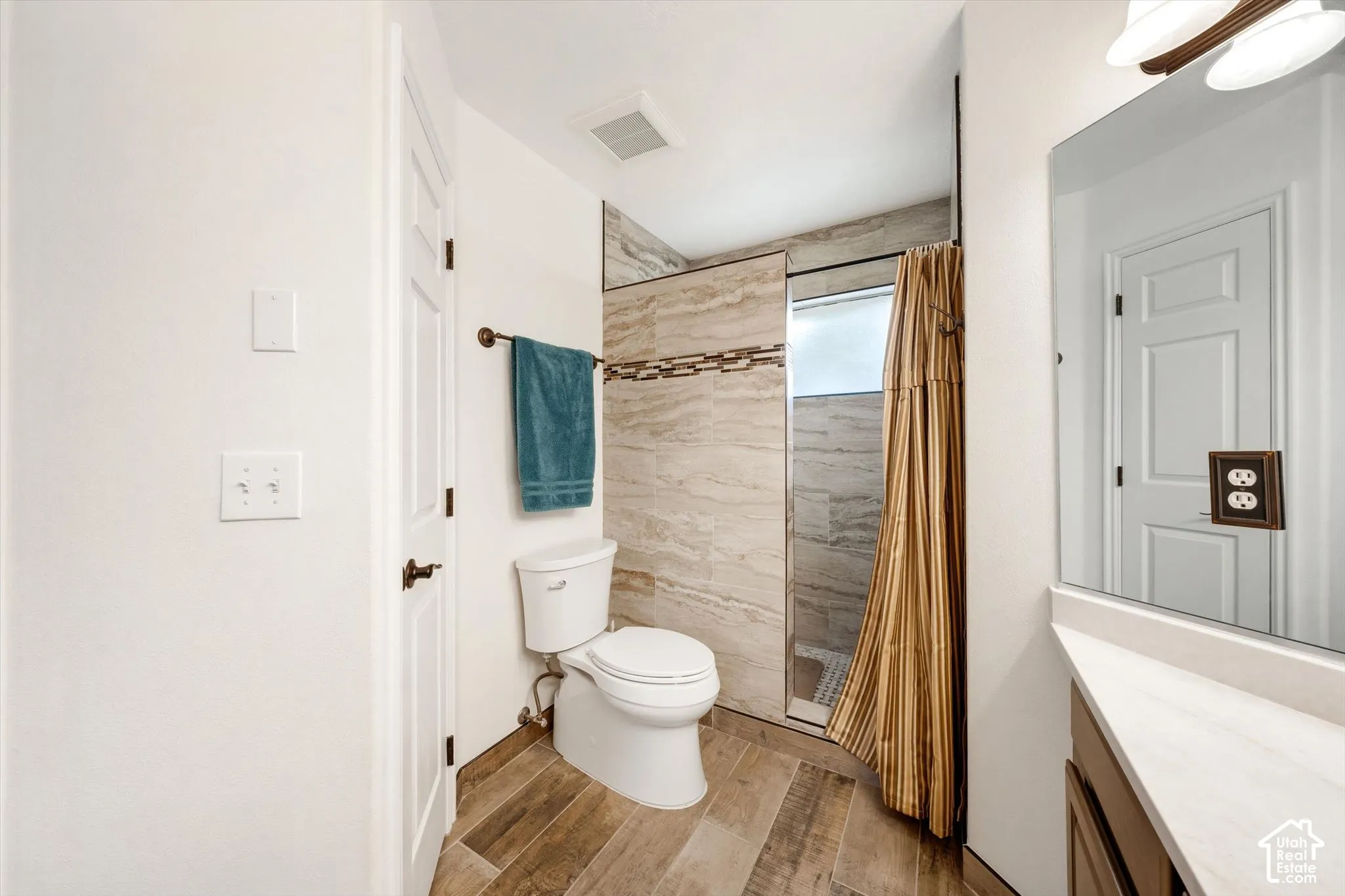 Bathroom featuring wood-finish flooring, a neutral-toned vanity with a light-colored countertop, and a tiled shower enclosure