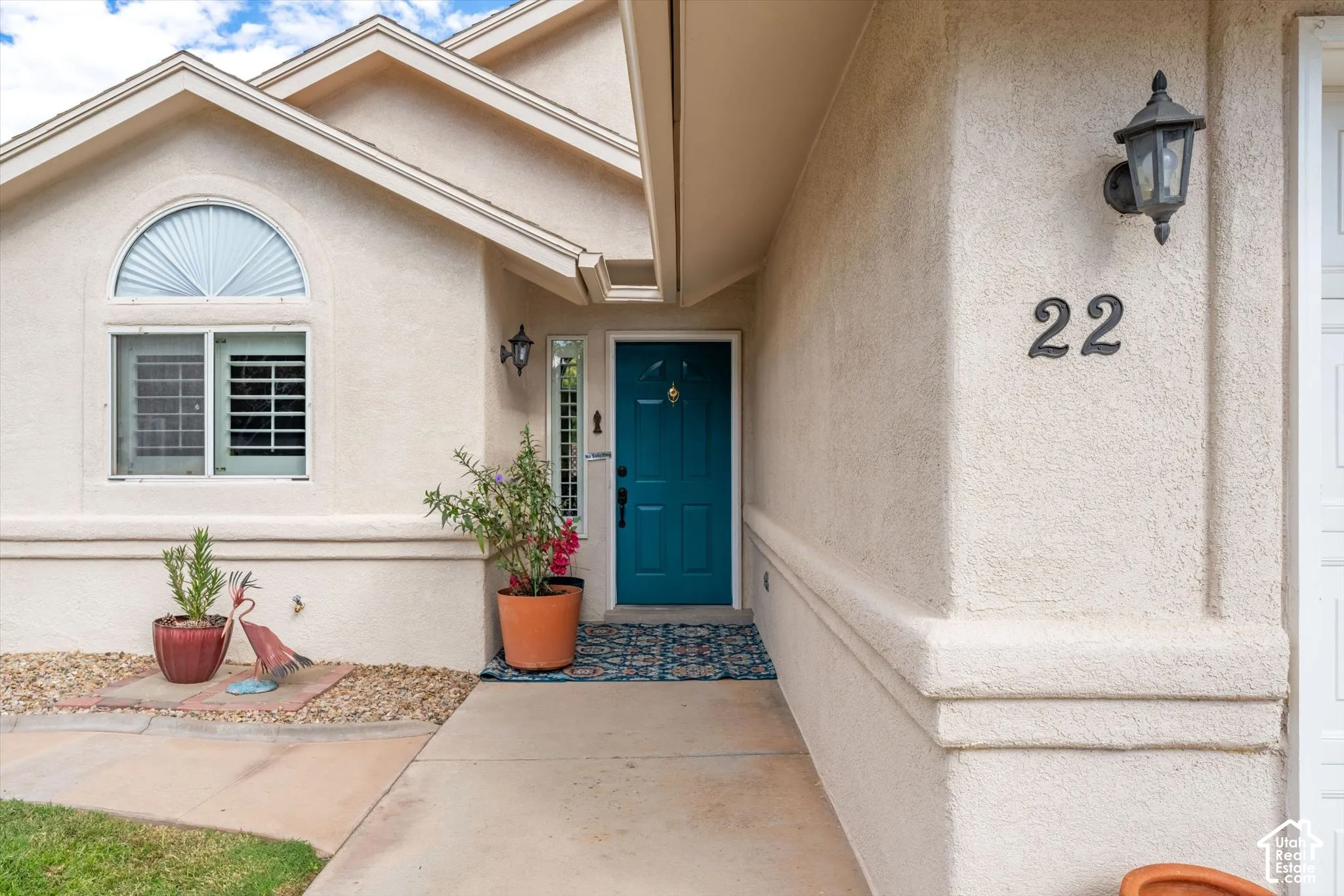 Stucco exterior with a peaked roofline, a vibrant teal entry door, a prominent arched window, and exterior lighting fixtures