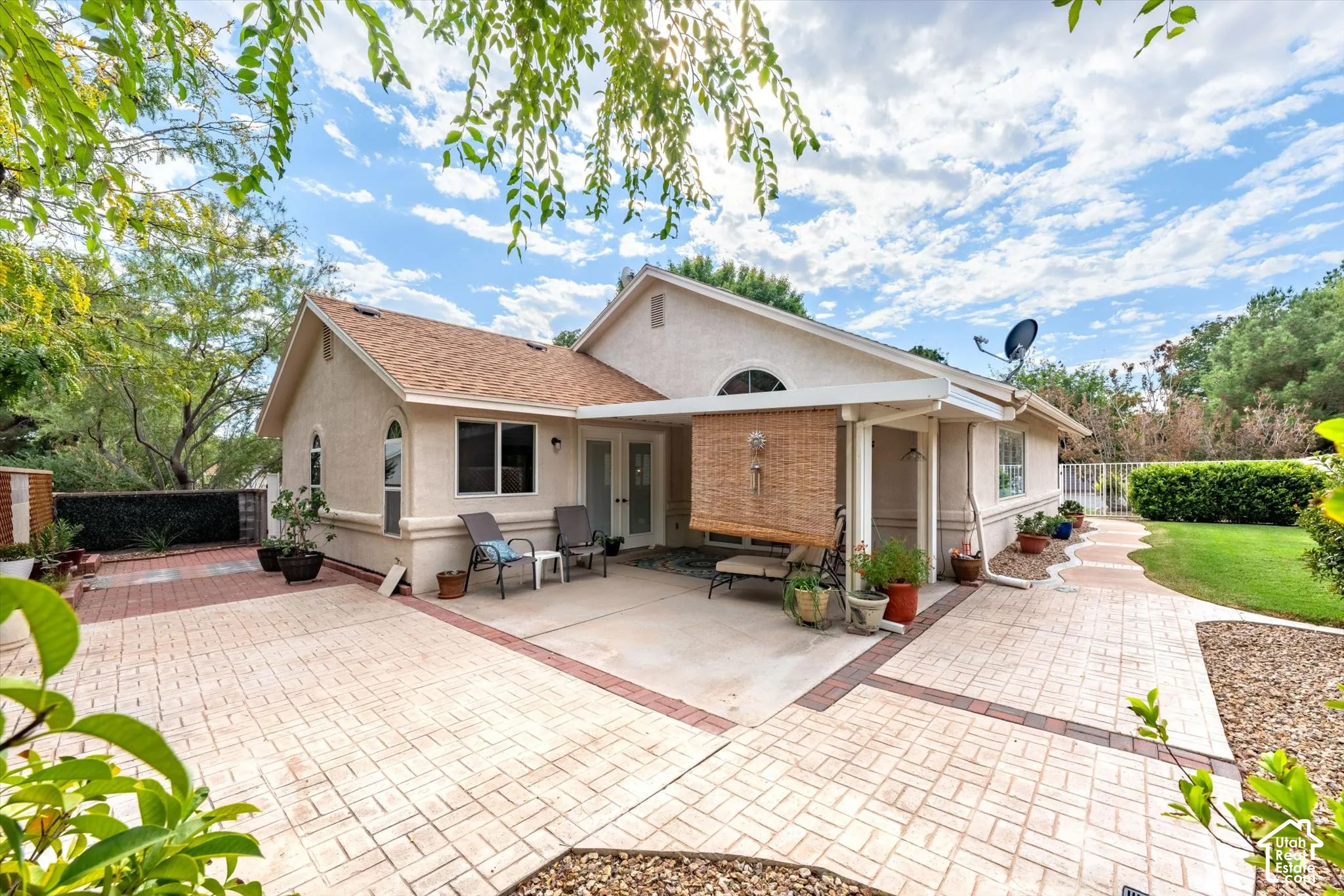 Stucco exterior with a covered patio, multiple windows, and a paved walkway