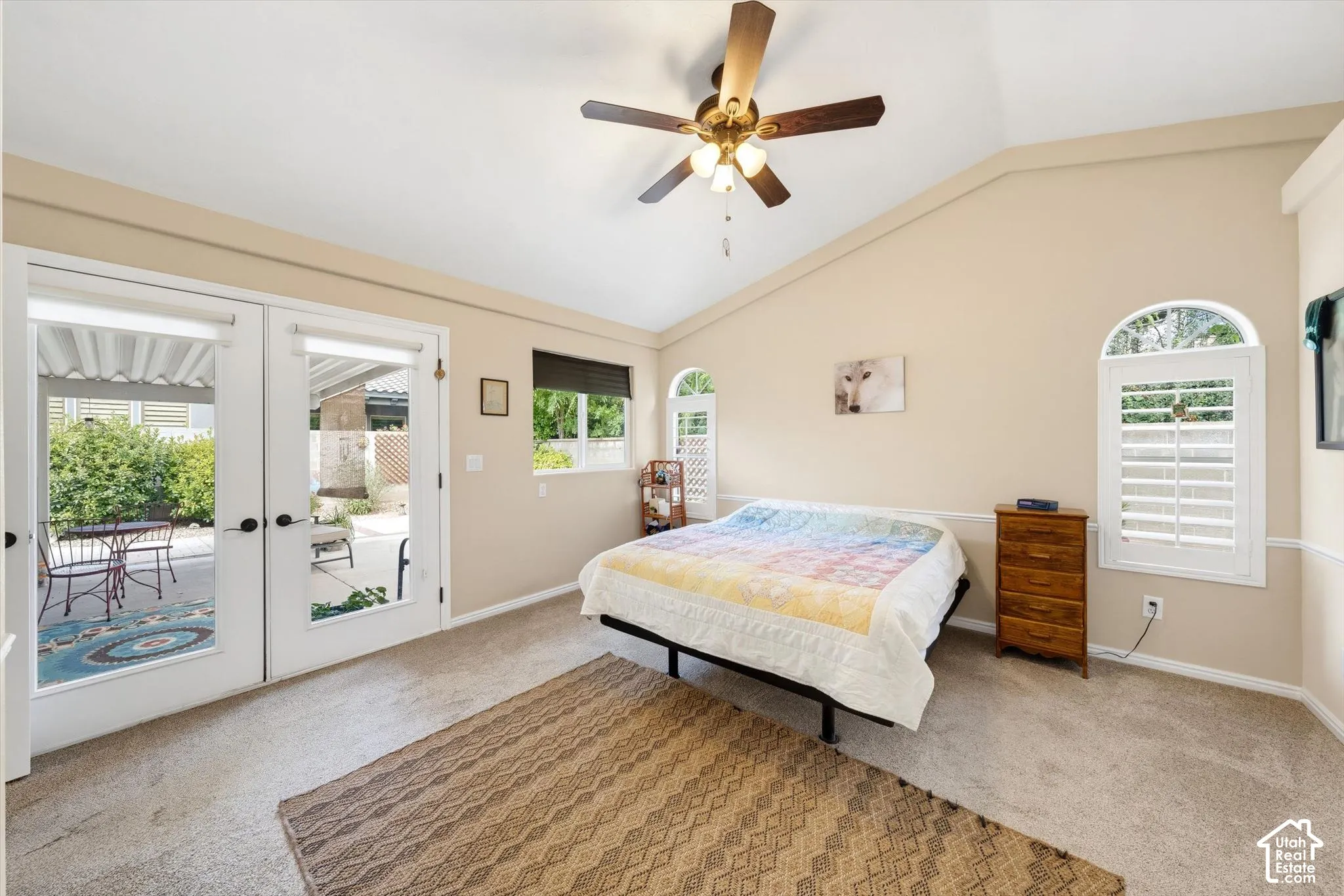 Vaulted ceiling with a ceiling fan, dual arched windows with plantation shutters, French doors, and soft carpeting