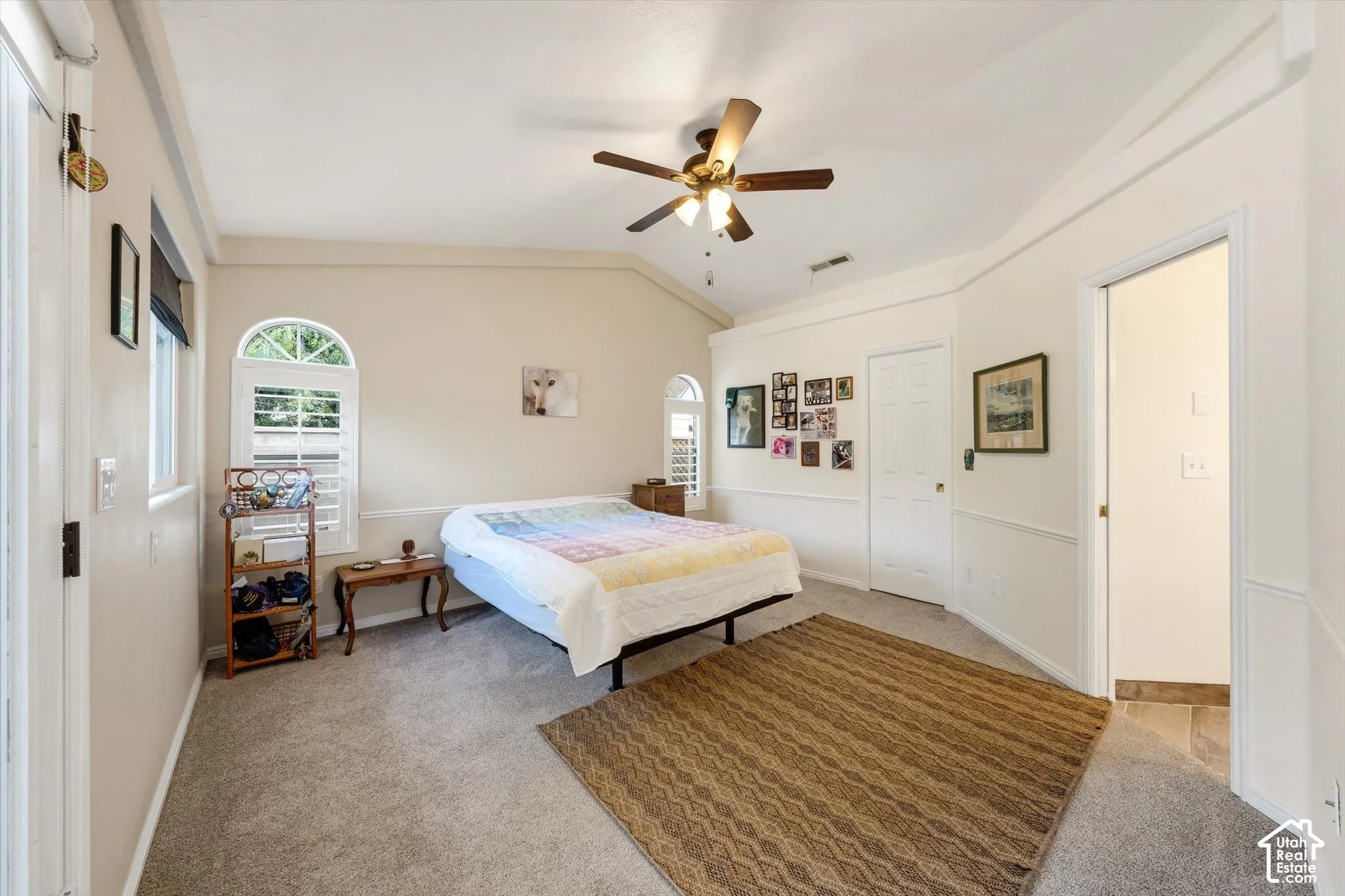Vaulted ceiling with an attached ceiling fan, arched windows with plantation shutters, wainscoting, and carpet flooring