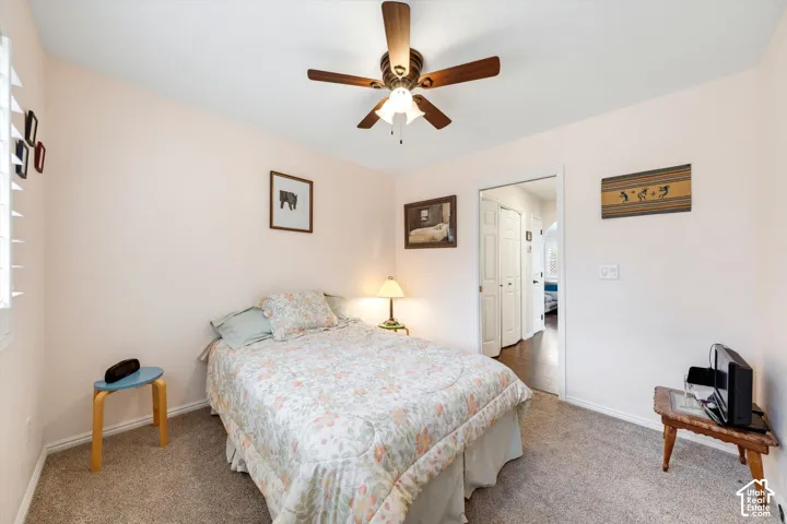 Carpeted flooring, ceiling fan with light fixture, window with louvered blinds, and a doorway with a panel door