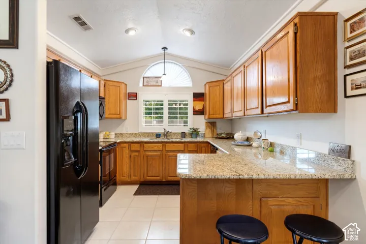 Kitchen featuring wood cabinetry, granite-style countertops, tile flooring, and a vaulted ceiling with recessed lighting