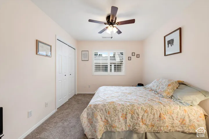 Wall-to-wall carpeting, window with plantation shutters, ceiling fan with integrated lighting, and bi-fold closet doors