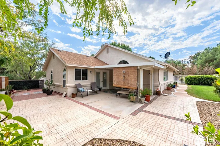 Stucco exterior with a covered patio, multiple windows, and a paved walkway