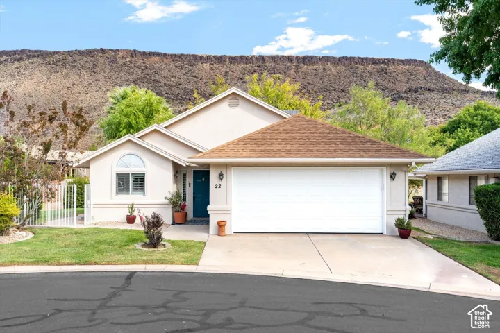 Stucco exterior with a pitched shingle roof, integrated two-car garage, manicured lawn, and a prominent mountain backdrop