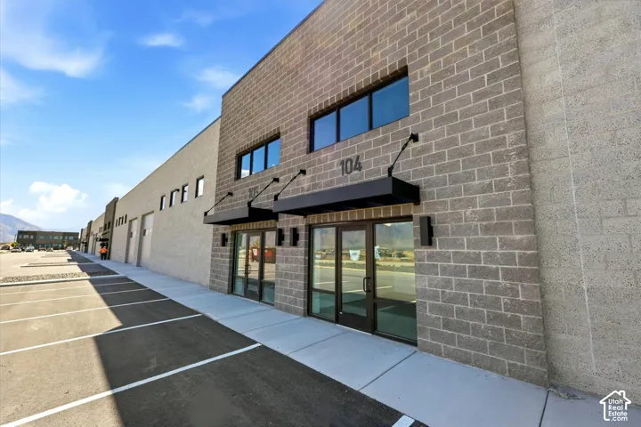 Gray brick facade with black awnings, prominent building numbers, large storefront windows, and dedicated parking