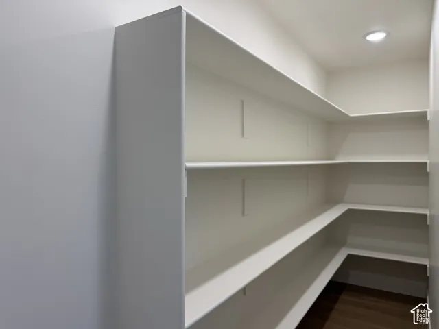 Expansive corner pantry featuring white shelving, a recessed ceiling light, and wood-finish flooring