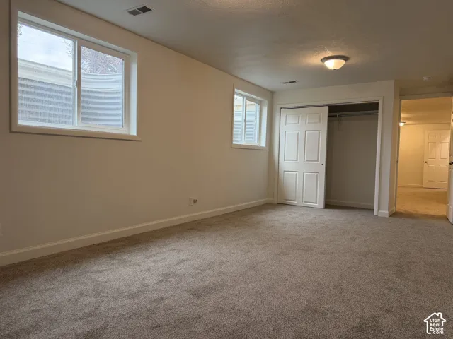 Plush carpet flooring, white painted walls, two windows, bi-fold closet doors, and an overhead light fixture