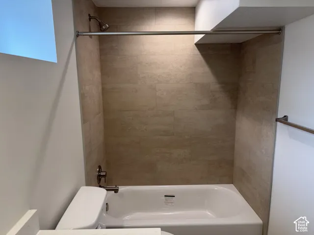 White bathtub with a brushed nickel shower head and fixtures, surrounded by large format beige wall tiles
