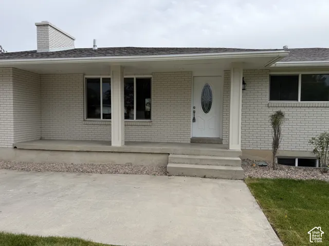 Light-colored brick exterior with multiple windows, a covered concrete porch, and a white front door featuring an oval glass insert