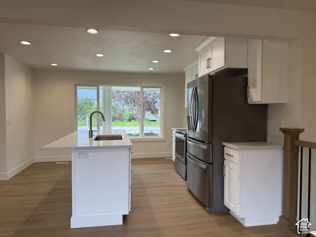 Kitchen featuring a center island with a stainless steel sink, white cabinetry, integrated stainless steel appliances, and wood-finish flooring