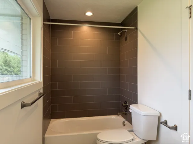 Bathtub with subway tile surround, white toilet, and matte black hardware