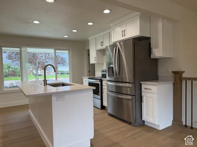 Kitchen featuring white cabinetry, stainless steel appliances, a center island with sink, quartz countertops, and wood-finish flooring