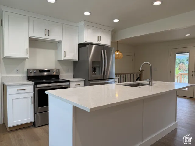 White shaker cabinetry, light-toned countertops, stainless steel appliances, recessed lighting, and wood-finish flooring