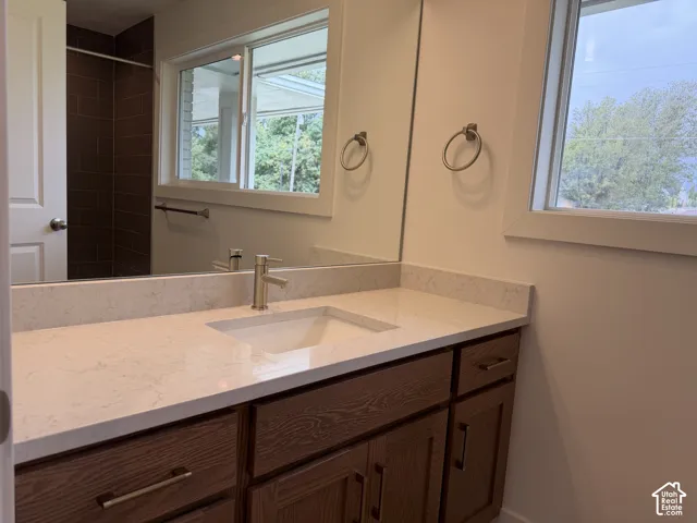 Wood-finish vanity with ample storage, integrated rectangular sink, light-toned countertop, and a window providing natural illumination