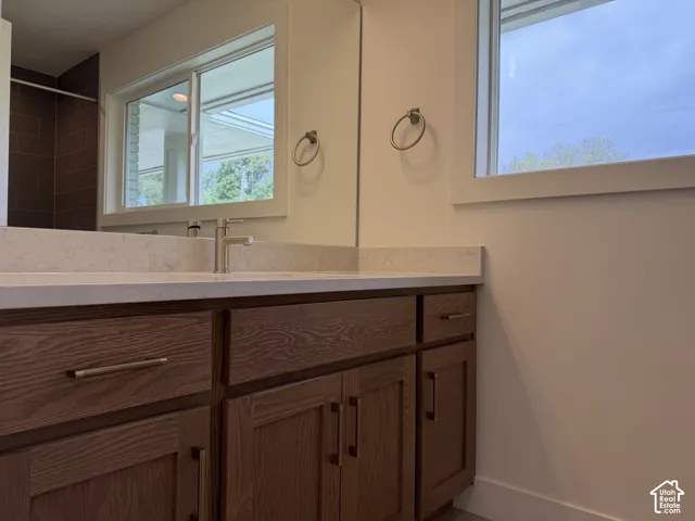 Wood-finish vanity with panel-front cabinetry, light-toned countertop, and undermount sink with a brushed nickel faucet