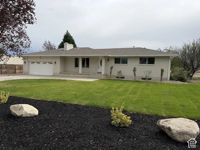 Ranch-style exterior with a two-car garage, concrete driveway, and a front yard featuring a manicured lawn and decorative landscaping