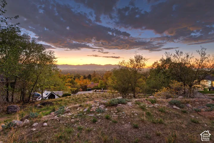 Expansive property featuring a sloped terrain, scattered rock formations, and mature trees, with a distant city skyline and mountain range