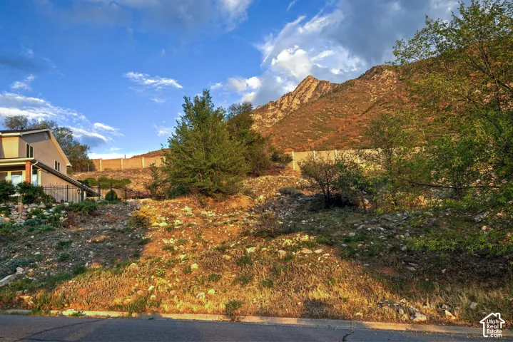 Sloped lot featuring partial fencing, mature trees, and natural landscaping with distant mountain scenery