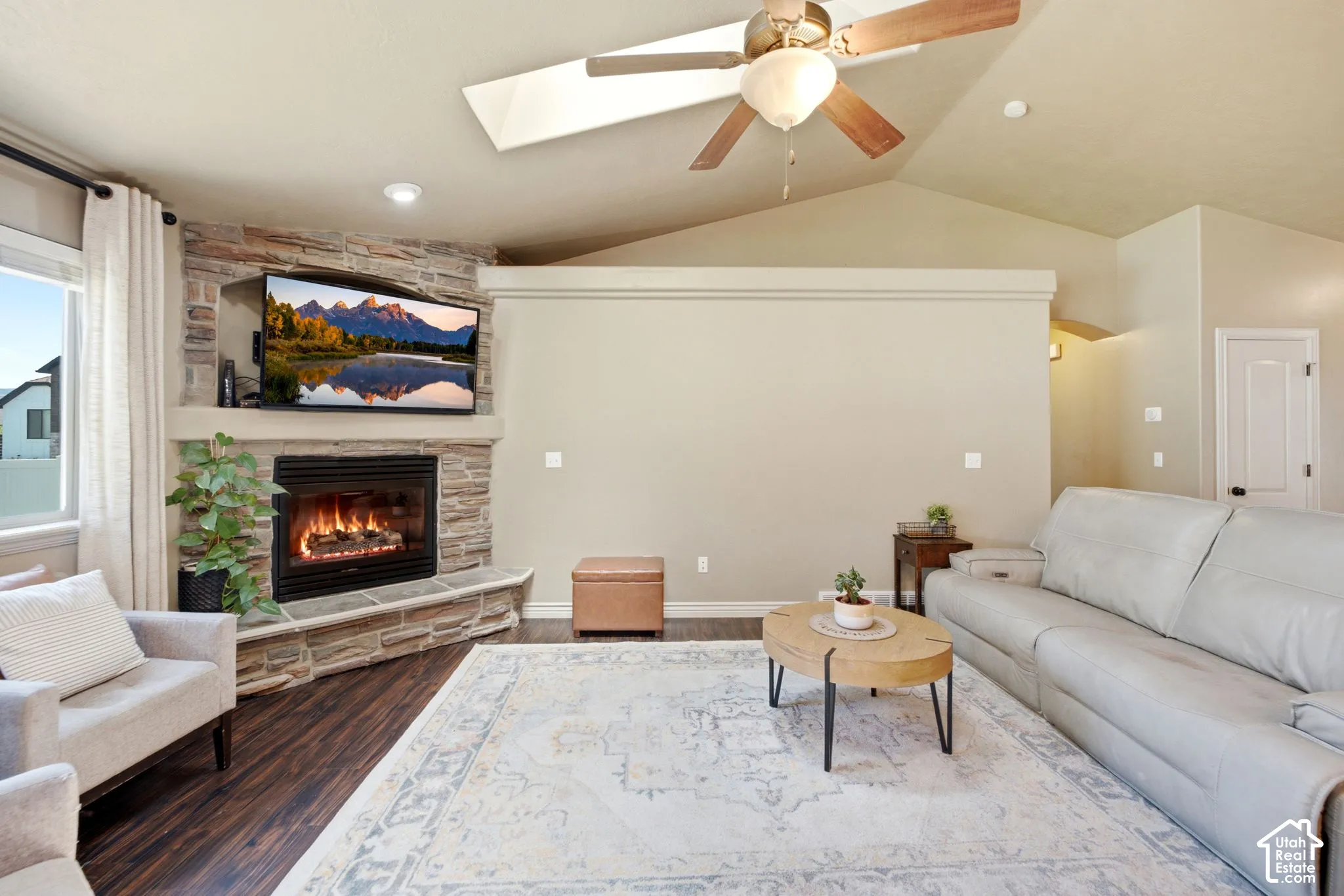 Living area featuring a corner stone-clad fireplace with a hearth, wood-finish flooring, vaulted ceiling with a ceiling fan, and recessed lighting